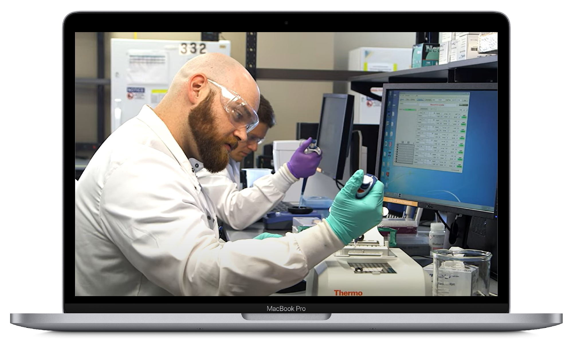 A MacBook Pro displaying a laboratory scene with two scientists working at computers and analyzing samples using lab equipment.
