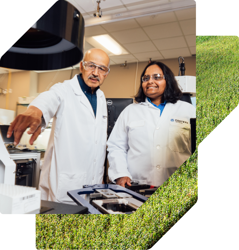 Two scientists in white lab coats and safety glasses work together in a bright laboratory, focusing on a piece of research equipment.