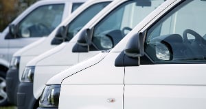A row of white commercial vans parked side-by-side, shown from a side-angle view.