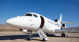 A sleek white private jet parked on tarmac with its boarding stairs deployed against a clear blue sky.