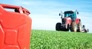 A red tractor in a green field under a clear blue sky, with a red fuel canister in the blurred foreground.